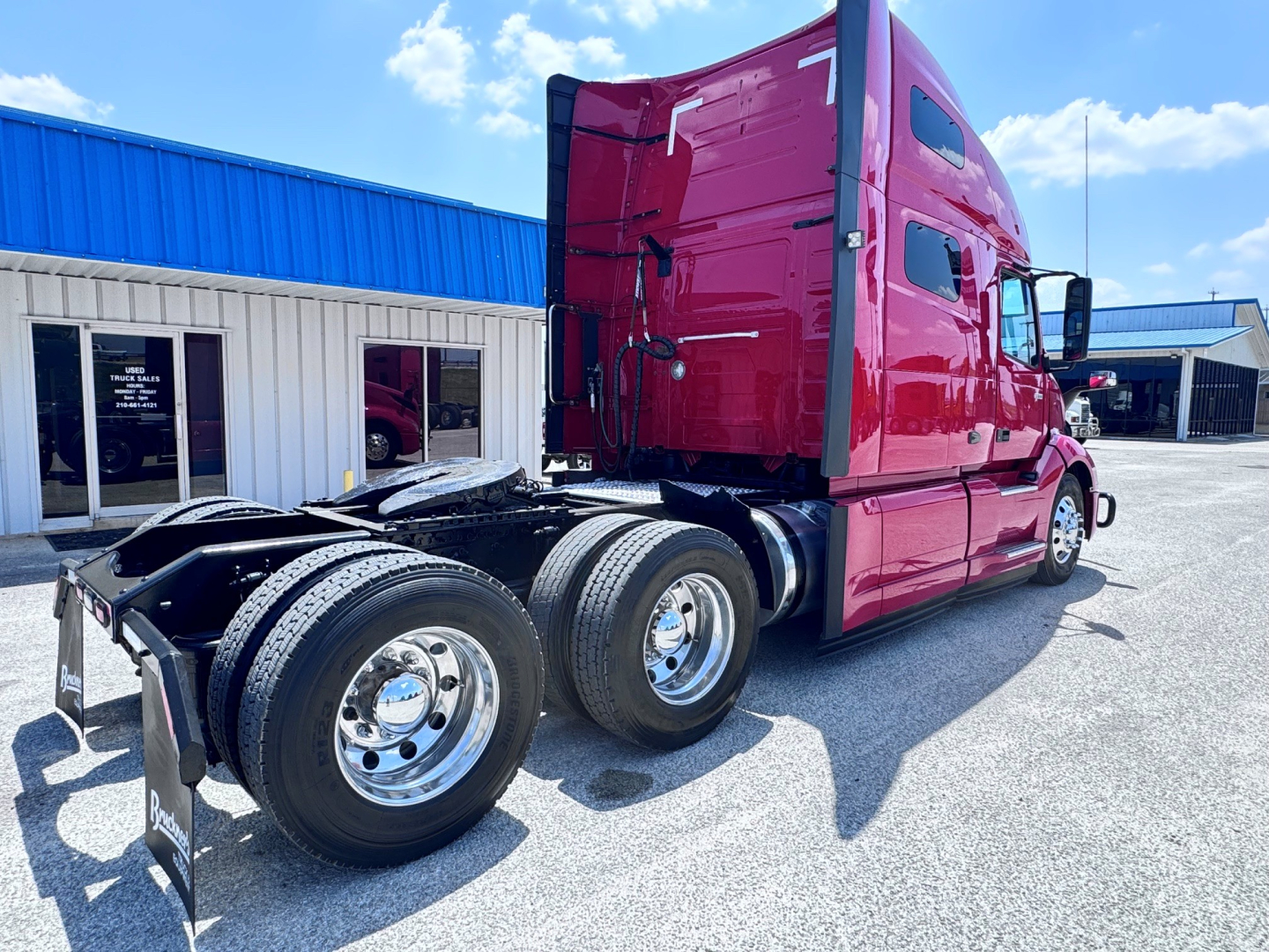 Truck cab and rear wheels of a red 2021 Volvo VNL64T760 tractor in a dealership lot, showing sleeper cab, DPF area, and dual rear axles.