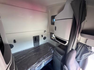 Cabin interior of a 2021 Volvo VNL64T760 sleeper truck showing bunk area with plastic-wrapped mattress, side wall panels, storage compartments, and window.