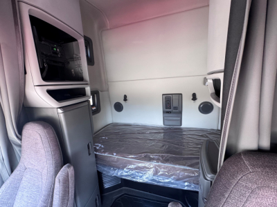 Cab interior of 2021 Volvo VNL64T760 sleeper showing bunk bed with plastic covering, side storage, dashboard switch panel, and windowed rear wall.