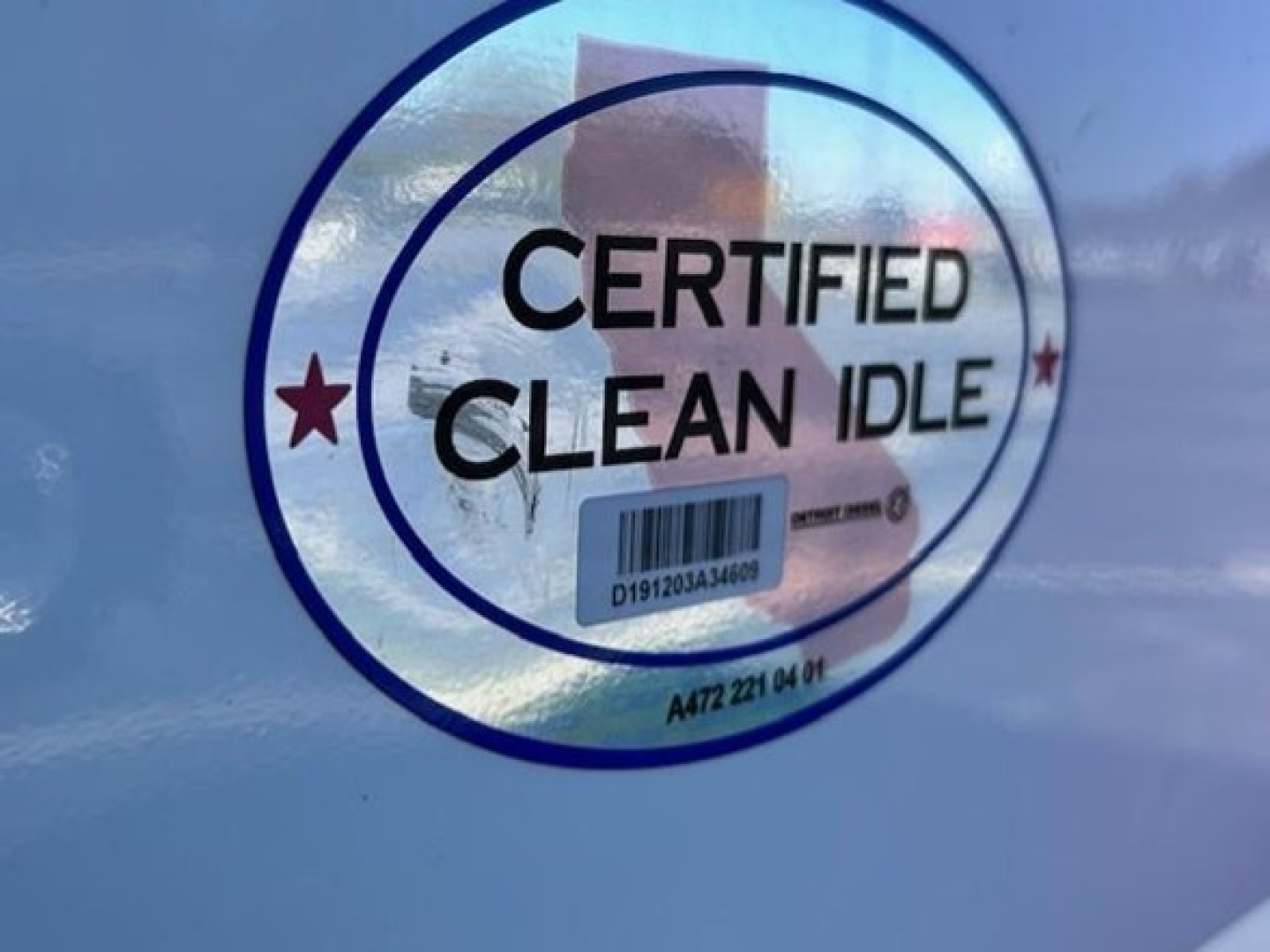 Certified Clean Idle sticker on blue Freightliner truck door, circular badge with barcode and text.