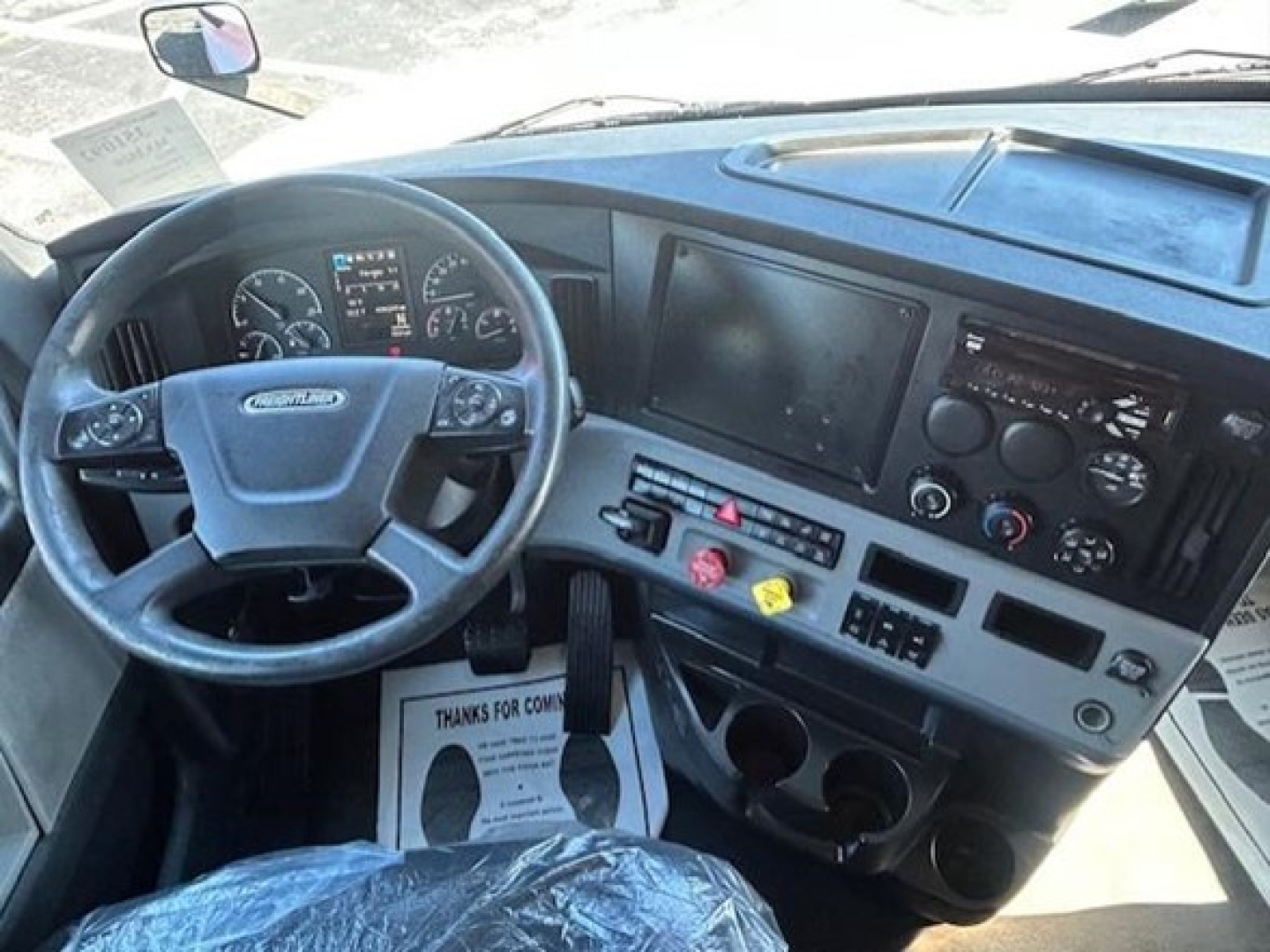 Cab interior of a Freightliner Cascadia 126 truck showing steering wheel, dashboard gauges, large touchscreen display, center controls, and cup holders.