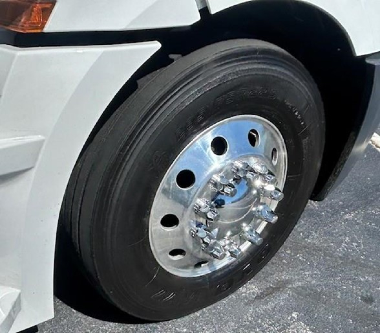 Front wheel of a Freightliner Cascadia 126 showing a steel hub with lug nuts and black tire, part of a white truck fender.