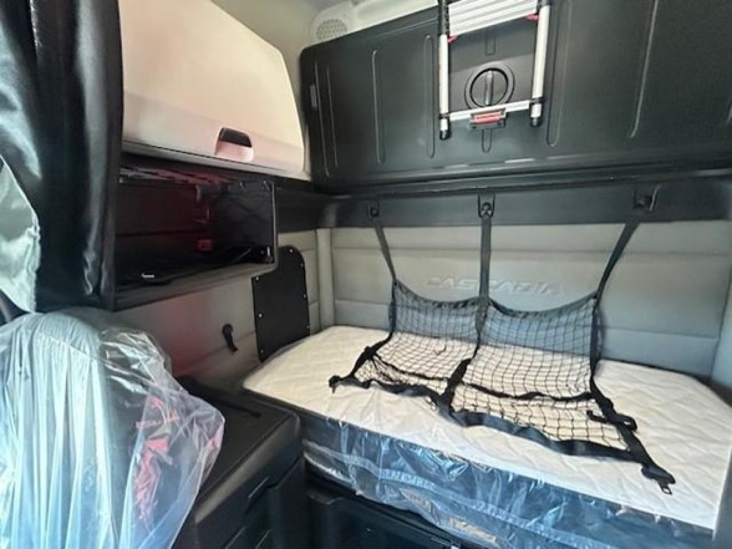 Freightliner Cascadia 126 sleeper cab interior showing bunk bed with netting and storage compartments.