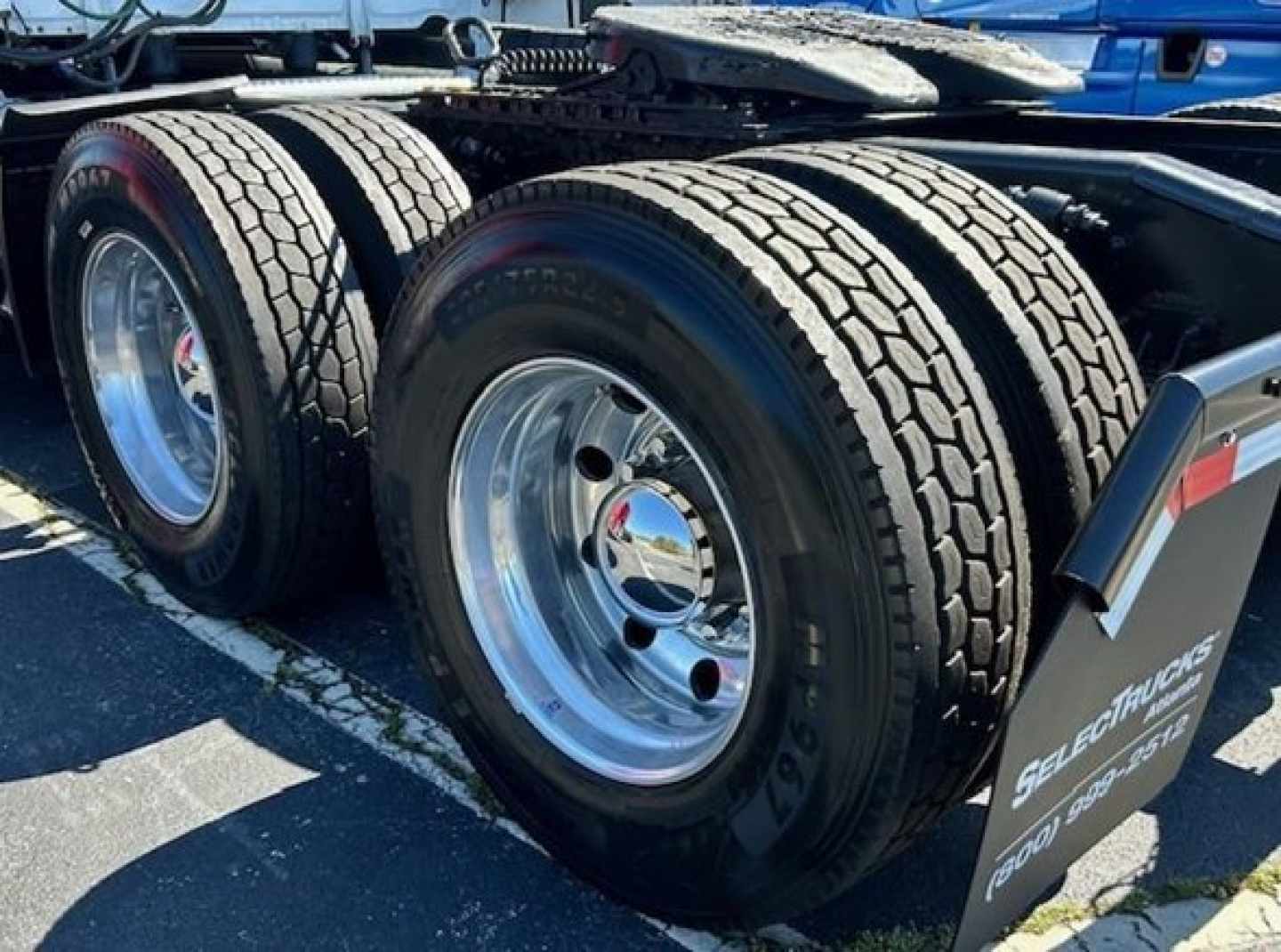 Freightliner Cascadia truck rear dual wheels with chrome rims and mud flaps; visible tire treads, undercarriage, and wheel area.