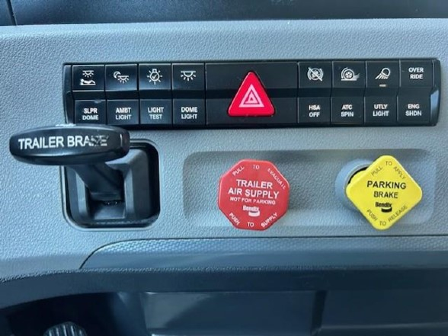 Dashboard panel of 2022 Freightliner Cascadia 126 showing hazard button, trailer brake control, and two reservoir caps (red trailer air supply, yellow parking brake) with labeled text.