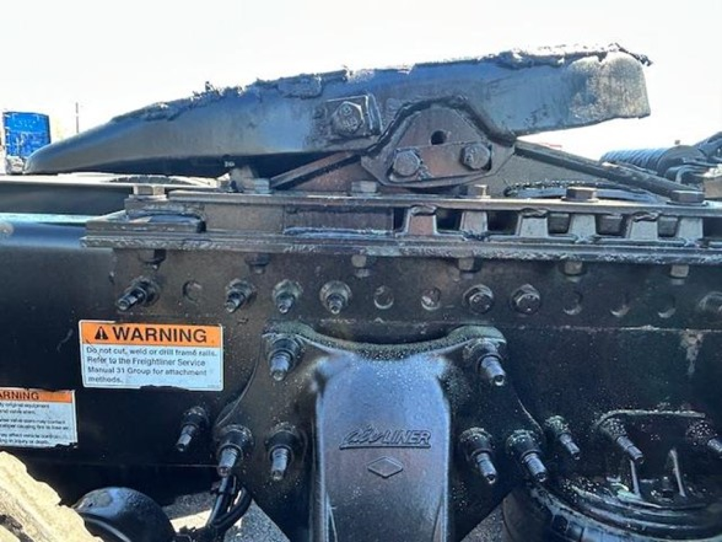 Tractor-trailer hinge area of a Freightliner Cascadia showing hydraulic lines and a component with the word 'LAVIA' or similar embossed on a metal bracket; warning label stickers visible.