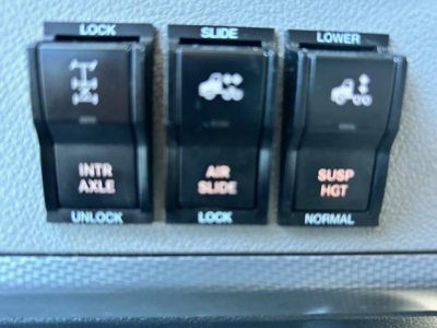 Truck interior control switches showing LOCK/UNLOCK, SLIDE, LOWER with icons for mirrors or windows and suspension; no other labels readable.