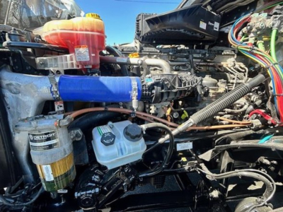 Freightliner Cascadia 126 engine bay showing coolant reservoir, blue silicone intercooler hose, diesel filter, and assorted wiring harnesses.