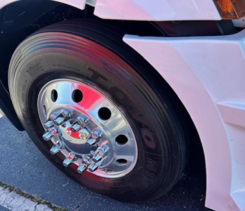 Wheel close-up of a Freightliner Cascadia 126 showing a polished chrome hubcap and tire with red reflections.