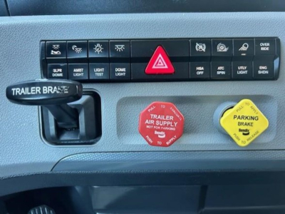 Dashboard panel of 2022 Freightliner Cascadia 126 showing hazard button, trailer brake control, and two reservoir caps (red trailer air supply, yellow parking brake) with labeled text.