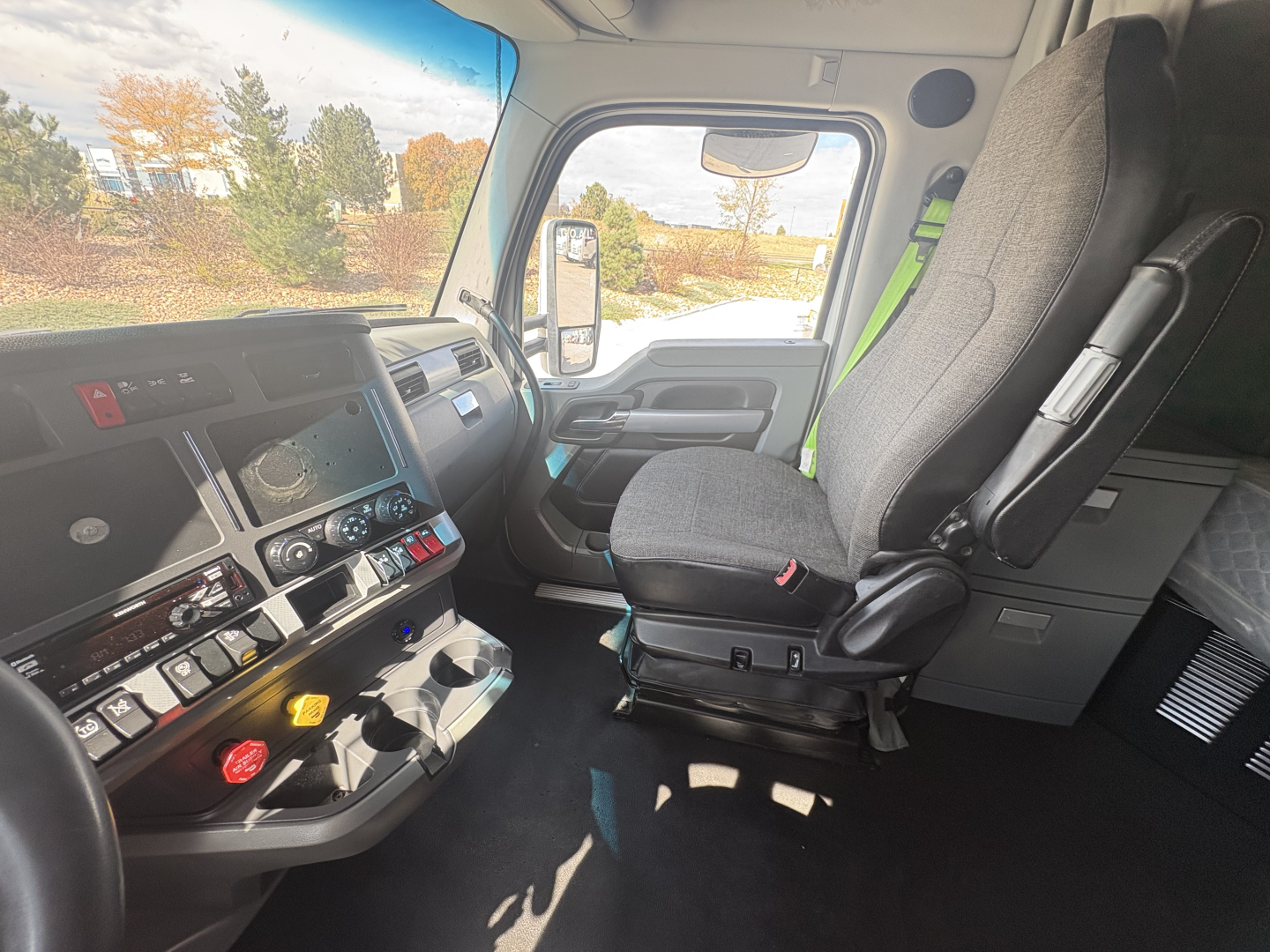Kenworth T680 cab interior showing driver seat, dashboard with gauges and controls, steering wheel, and large side door window.