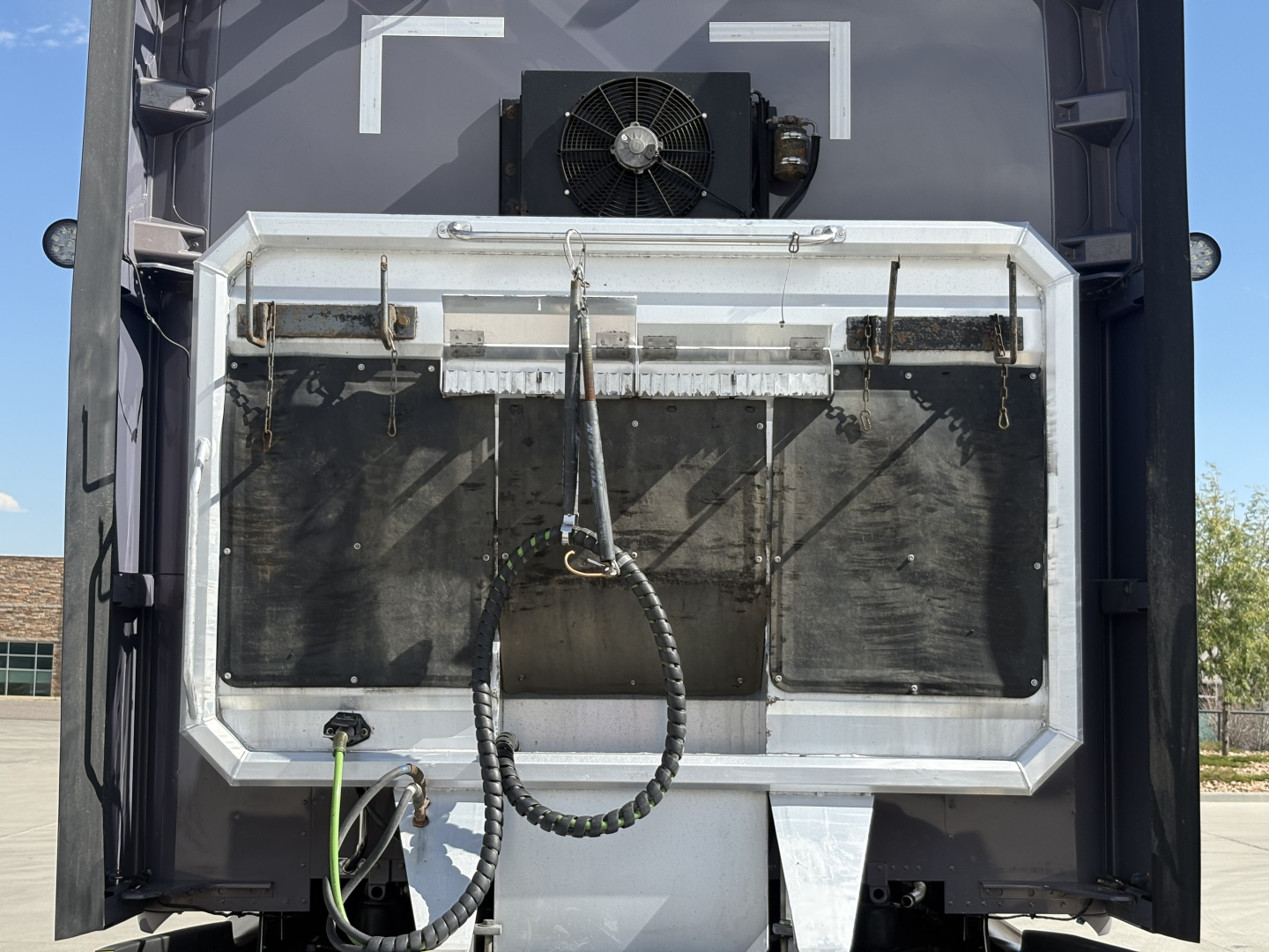 Kenworth T680 rear view showing radiator, license/step area and various hoses; black exterior with metal frame around rear opening.