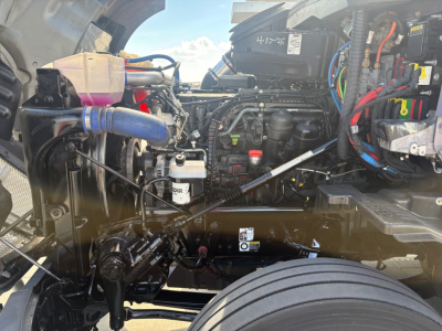 Kenworth T680 engine bay showing various hoses, wiring, and the radiator reservoir with translucent container.