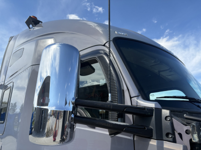 Kenworth T680 truck cab front angle showing chrome mirror, aerodynamic window, and grille area with blue sky reflection.