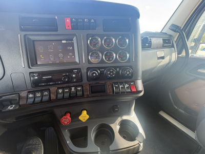 Dashboard of 2022 Kenworth T680 interior showing steering column center console with multiple gauges, touchscreen infotainment, climate controls, and red/yellow switches; cup holders visible.