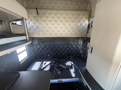 Truck cab interior showing sleeping area with quilted cream and black upholstery, storage compartments, and window.