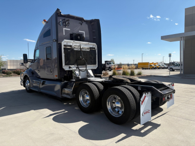 Kenworth T680 tractor rear view showing fuel tanks, dual rear axles, and chassis with attached fifth wheel in a truck lot.