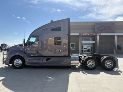 Kenworth T680 truck side view showing sleeper cab, attached 6x4 rear wheels, and dealership building in background.