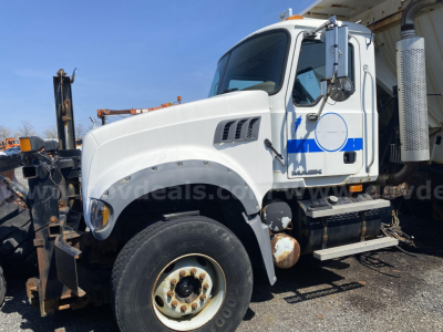 Truck cab side view showing Mack CTP713 dump truck with white paint and blue stripe, front wheel, exhaust stack, and equipment attachments.