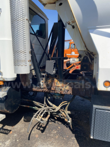 Truck engine bay area with hydraulic hoses and dump bed linkage visible between cab and dump body. Mack CTP713, side view, metal components, hoses, and brackets.