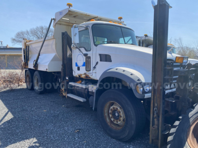 Truck cab and dump bed with front mount equipment and wheel, side mirror, headlights visible. Text visible on door and side panels includes company logo and small labels, but no legible serials or fluid labels.