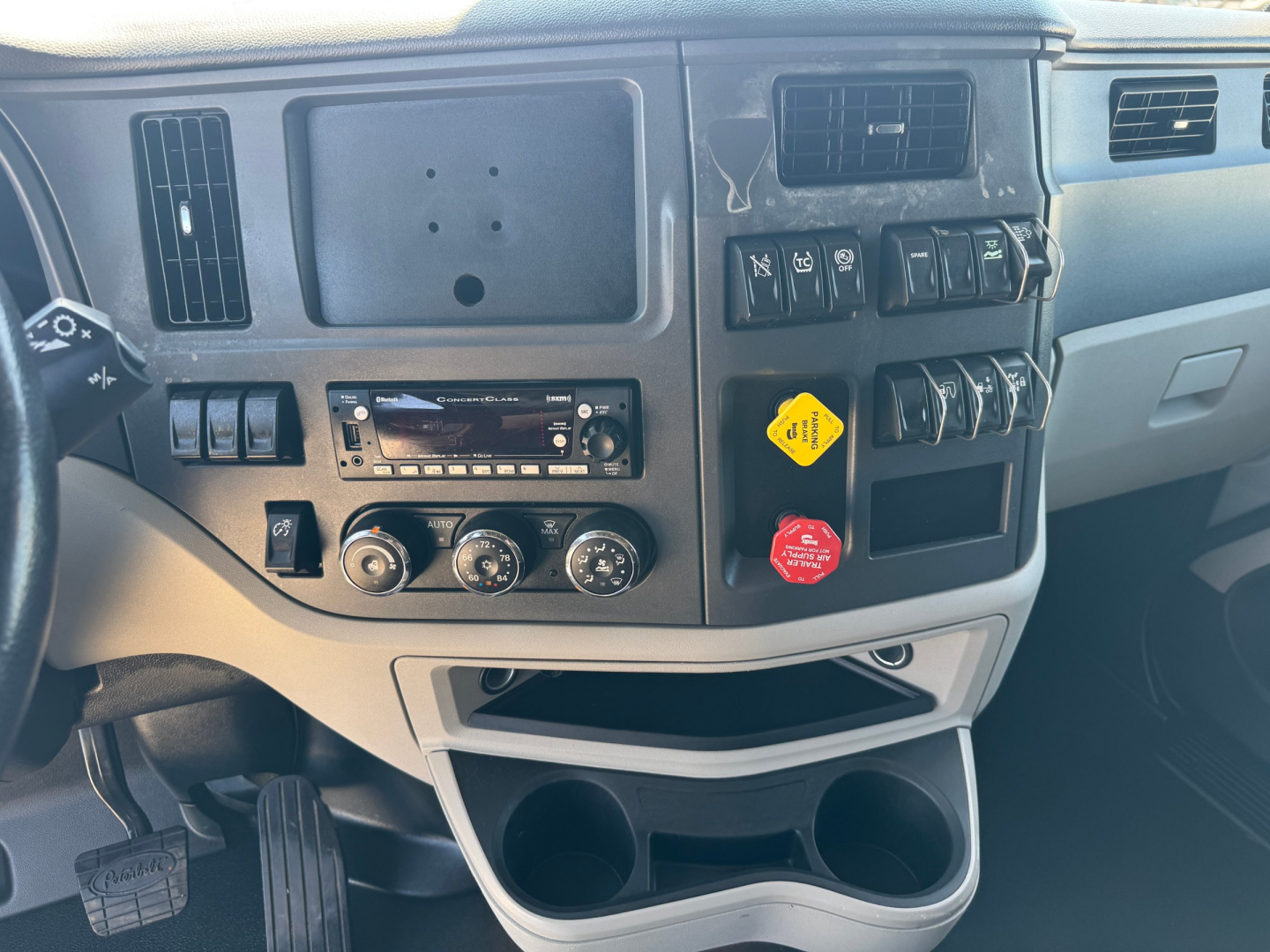 Peterbilt 579 dash area showing air vent panels, switches, climate controls, cup holders, and a yellow warning tag on the switch cluster.