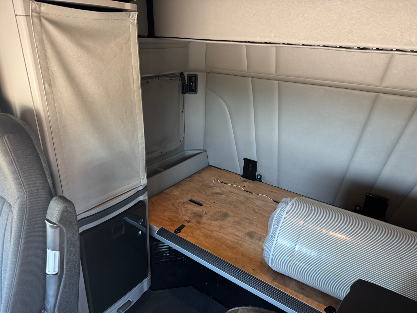 Peterbilt 579 sleeper cab interior cargo area with wooden floor platform and a cylindrical duct, view from side door opening.