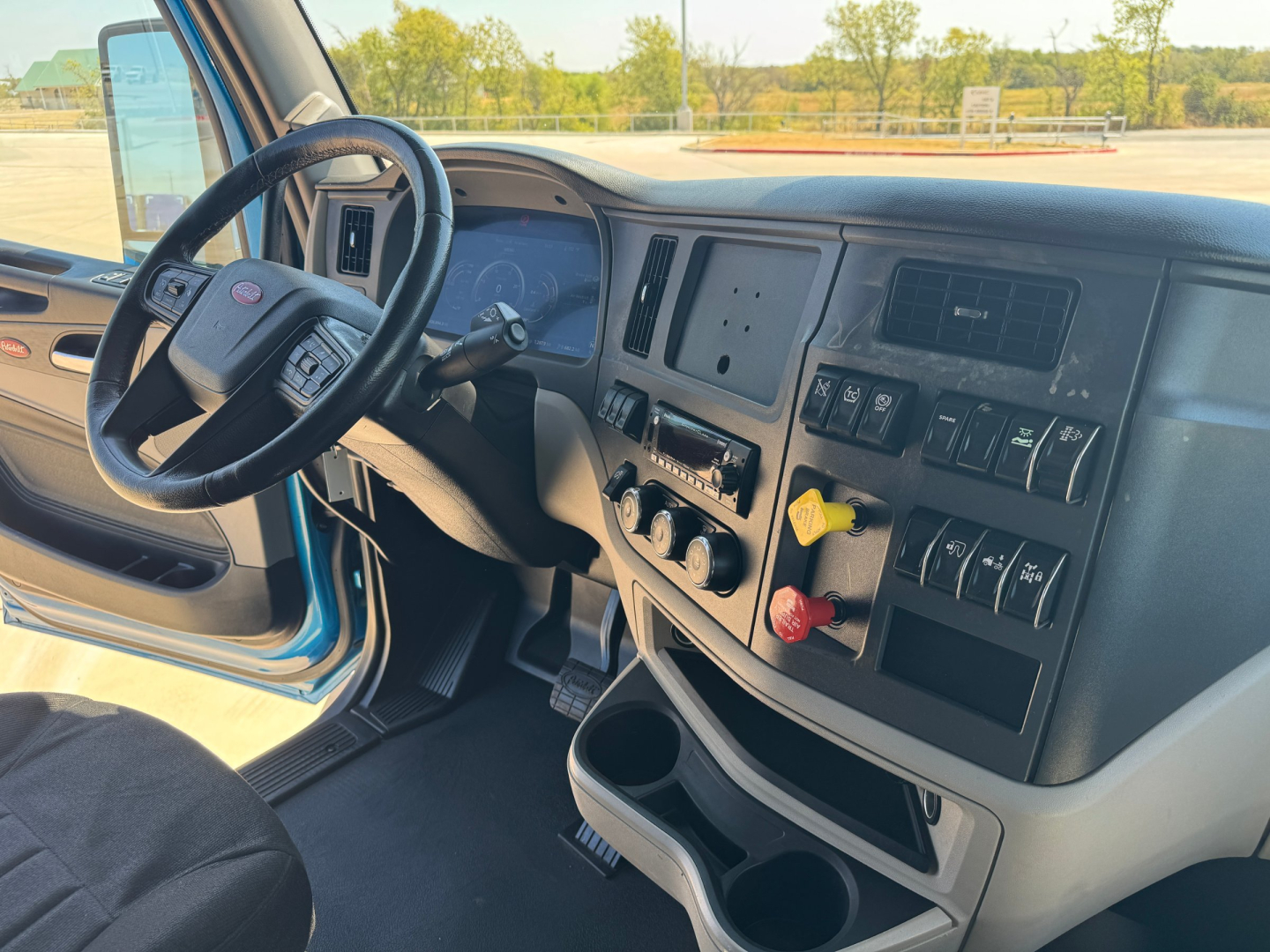 Peterbilt 579 interior dashboard and steering wheel showing center console with gauges and switches, driver-side door, and cup holders.