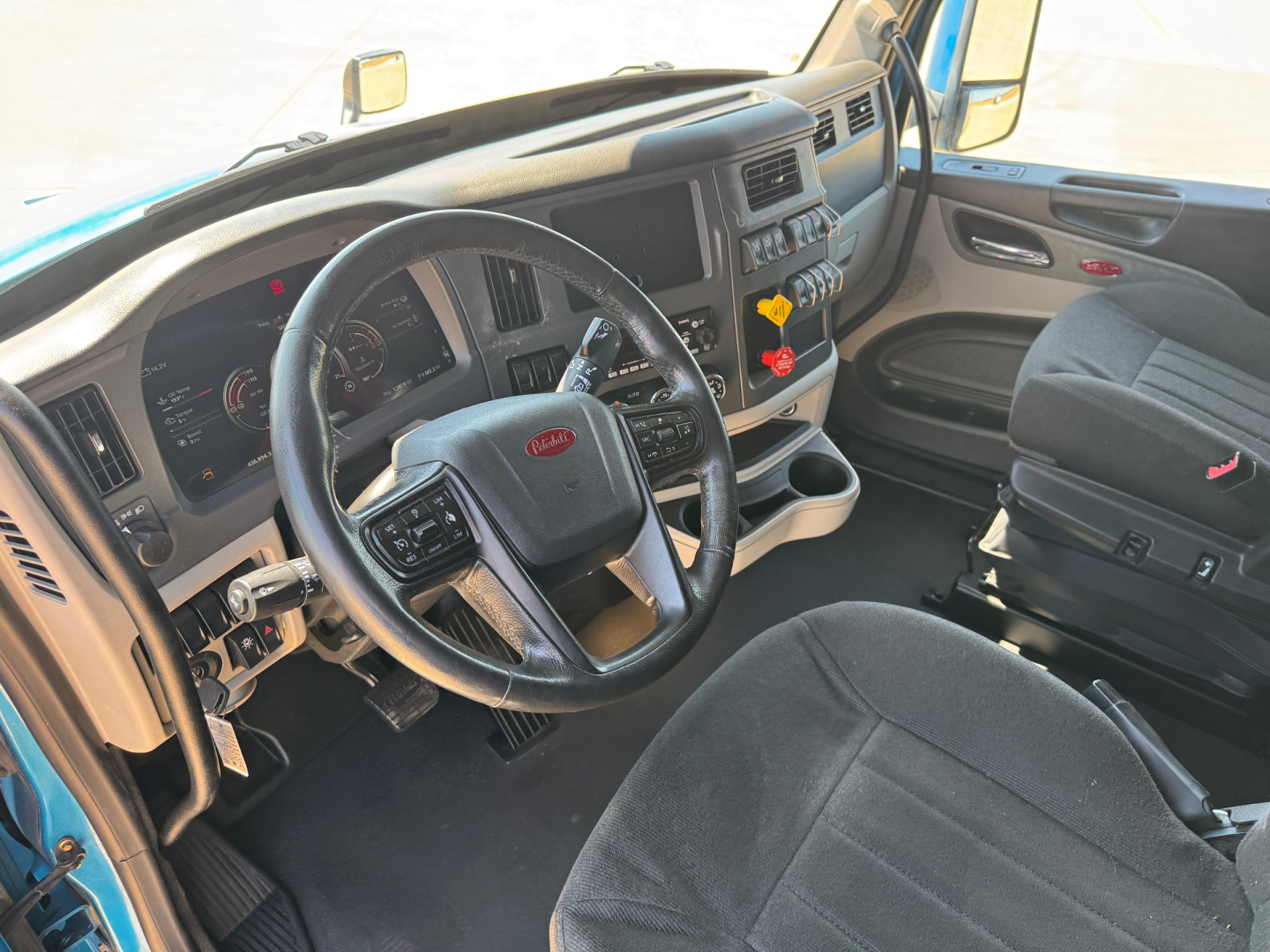 Peterbilt 579 cab interior showing steering wheel, dashboard, and driver seat with controls and switches.