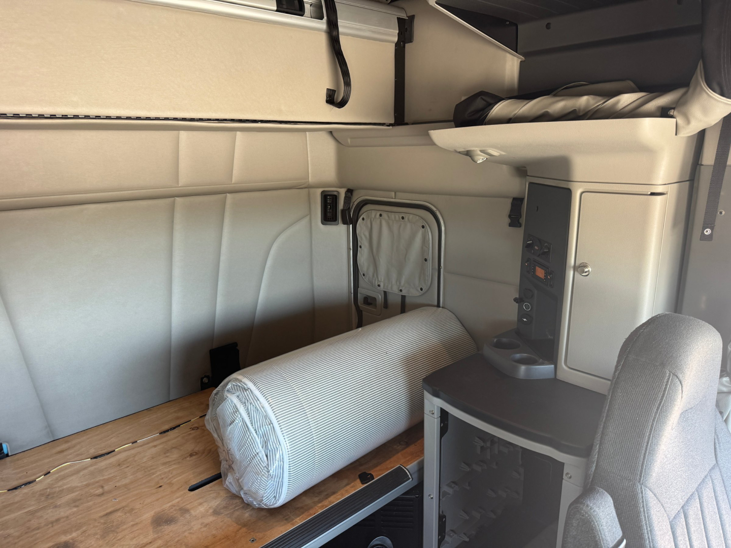 Peterbilt 579 sleeper cab interior showing storage area with a rolled mattress, cabinet, and control panel.