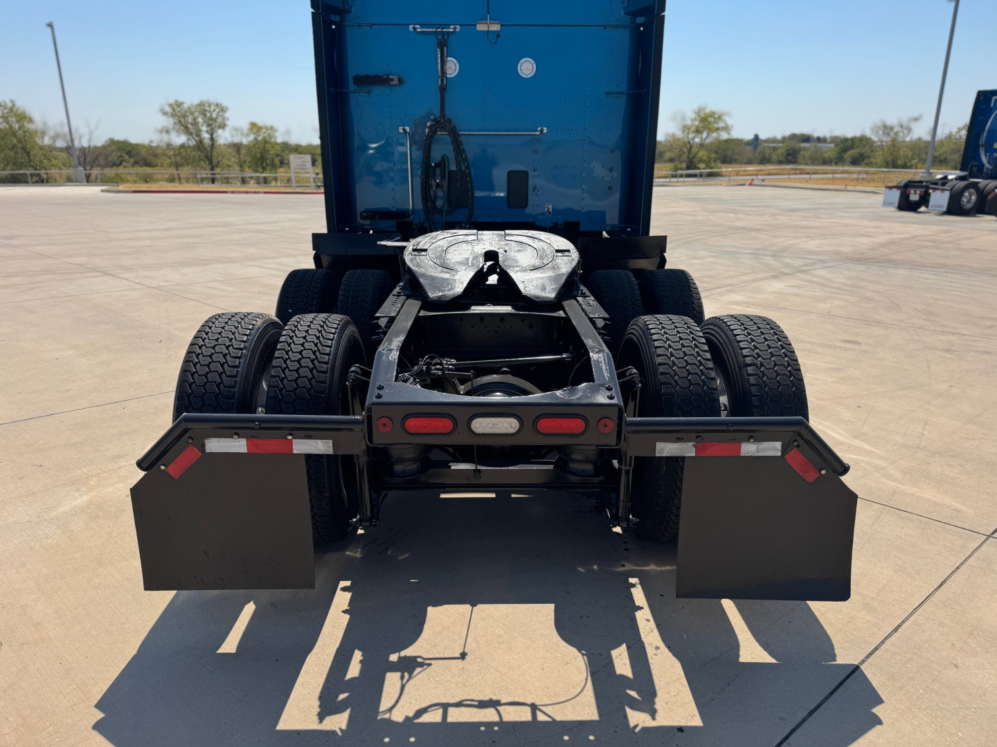 Truck rear view showing fifth-wheel coupling on a Peterbilt 579 tractor with dual rear axles and mud flaps.