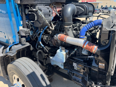 Peterbilt 579 engine bay with blue and black components, hoses, and a light blue coolant reservoir visible.