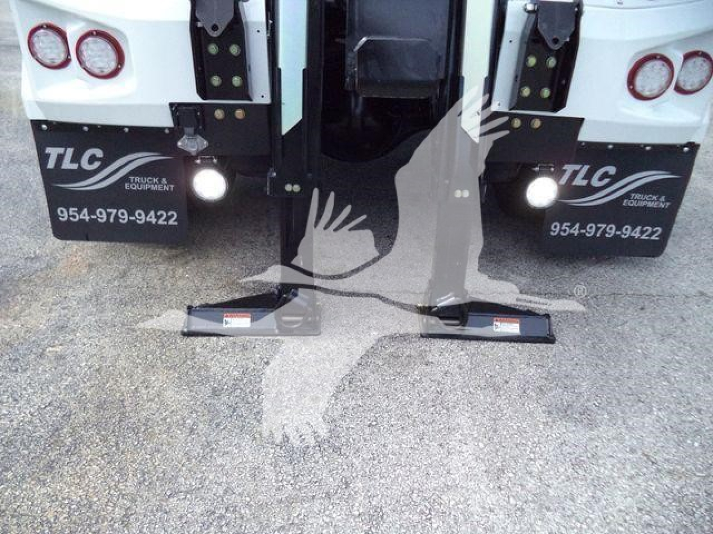 Image of the rear of a new 2025 International MV truck configured with a winch, showing dual mud flaps with TLC Truck Equipment branding and contact number, and ramp stubs at the ground.