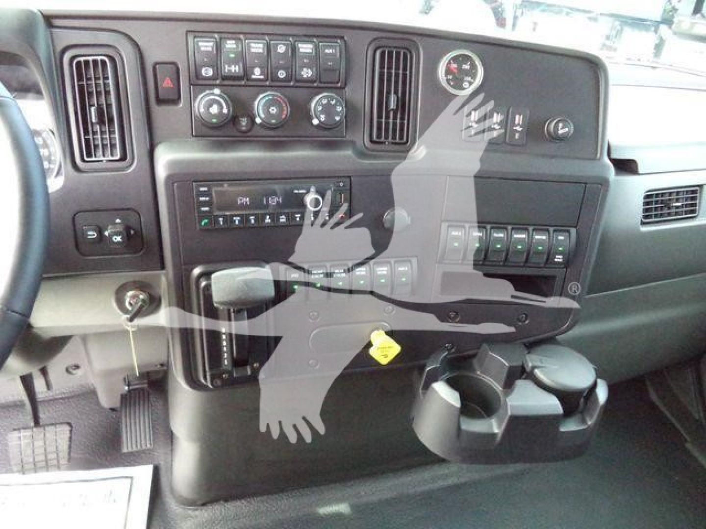 Interior dashboard of a 2025 International MV truck showcasing controls, gauges, and a cup holder. Visible items include steering column area, HVAC controls, radio, and various switch panels.