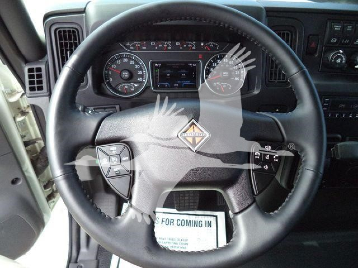 Steering wheel and instrument cluster of a 2025 International MV truck showing the MV diamond emblem and dashboard controls.