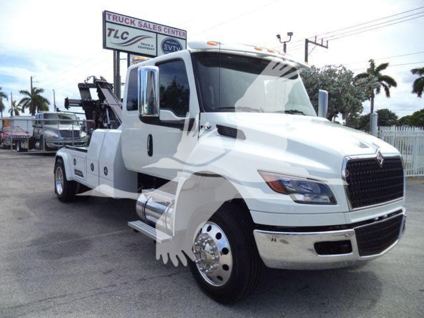 International MV tow truck in white showing front and side view with winch equipment in background.