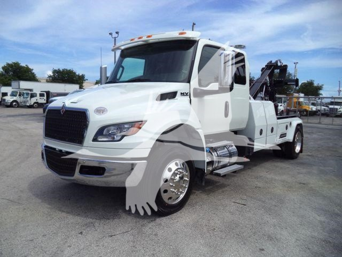 Tow truck with a white International MV cab and black tow winch apparatus in a dealership lot; side view showing chrome steps and wheel well details.