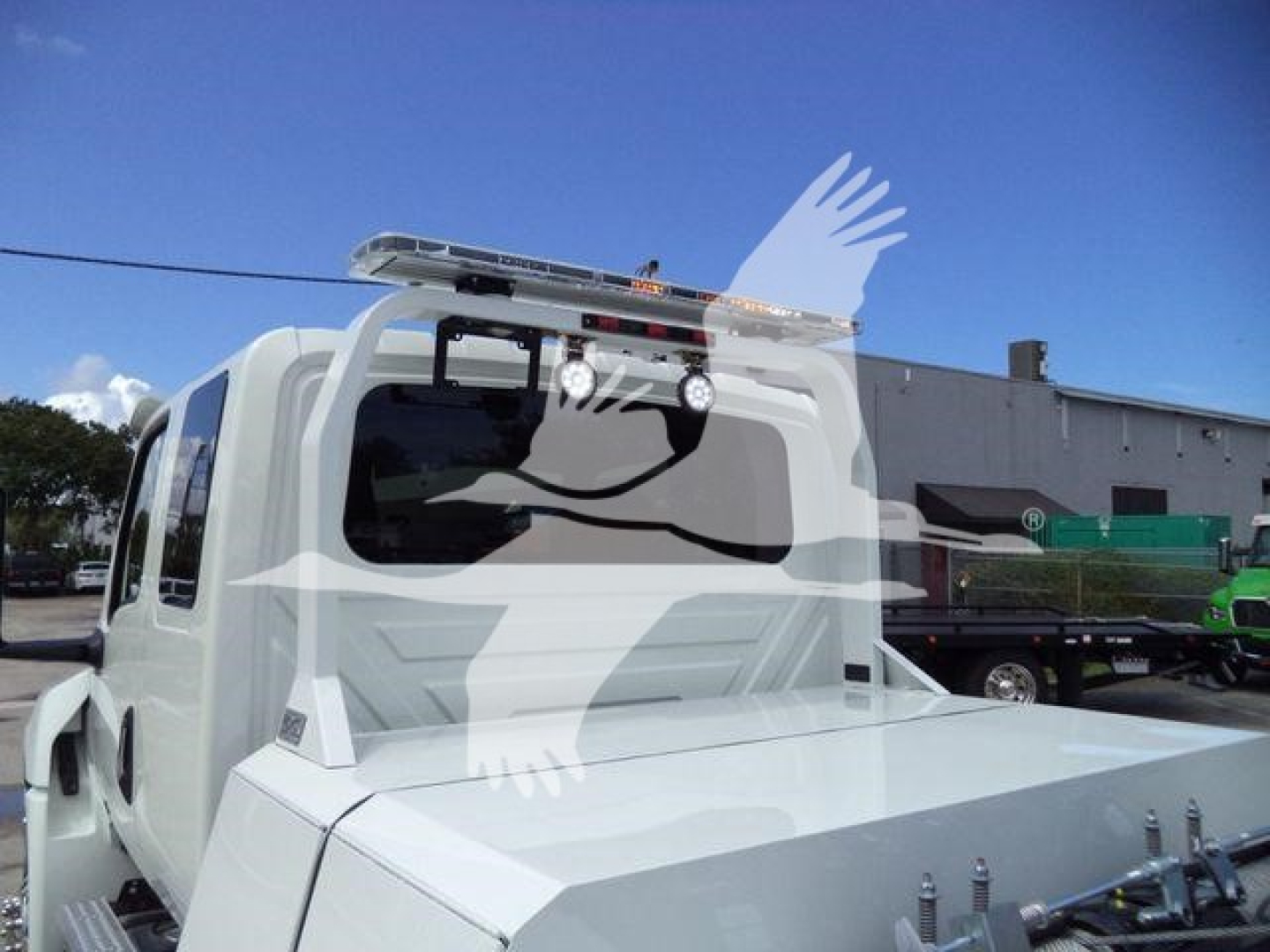 Truck cab rear view showing roof-mounted cargo light bar and flatbed with tie-down lugs.