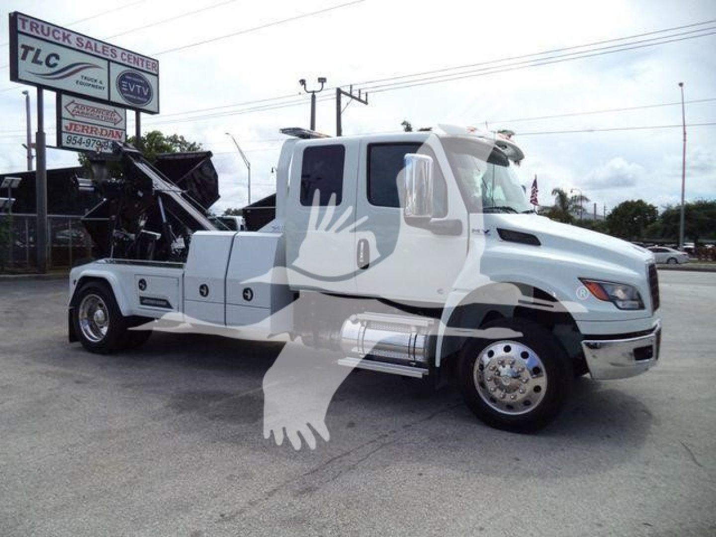 White heavy-duty International MV truck with a winch, front grille, dual rear wheels visible, side compartments, and a sign in background.