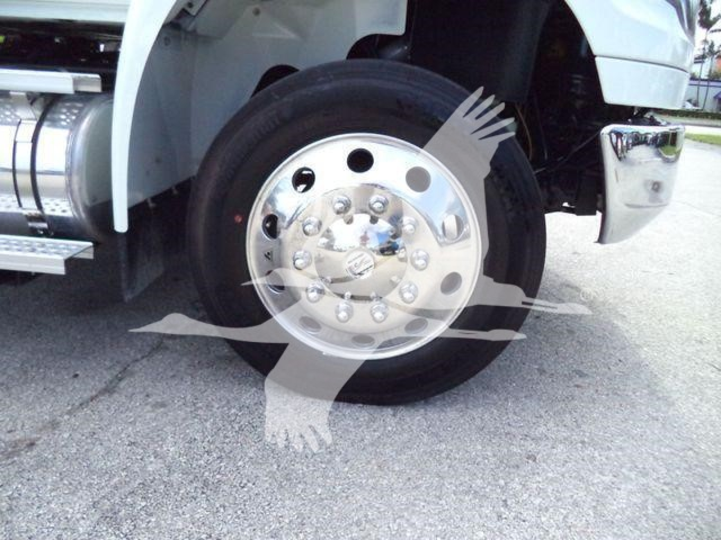 Wheel and tire assembly of a white International MV truck showing hubcap with lug nuts and chrome details, front fender, and part of chrome bumper.