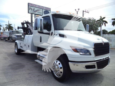 International MV tow truck in white showing front and side view with winch equipment in background.