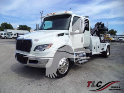 Truck showing International MV tow truck with winch and hook lift, white cab, side steps, chrome fuel tanks, and black grille.