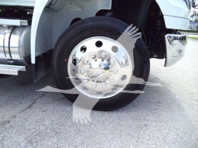 Wheel and tire assembly of a white International MV truck showing hubcap with lug nuts and chrome details, front fender, and part of chrome bumper.