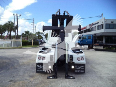 Truck with heavy-duty vertical winch mounting and accessory hooks mounted between two white cab-forward trucks; rear view shows winch assembly and lifting hooks.