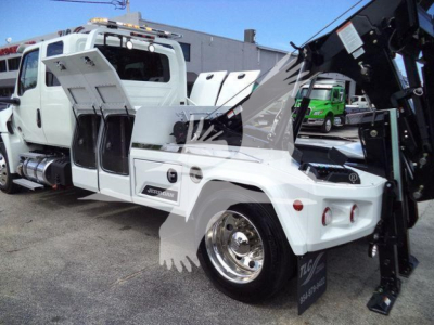 International MV winch truck showing open side compartments and crane arm in operation with white body and chrome wheel hub.