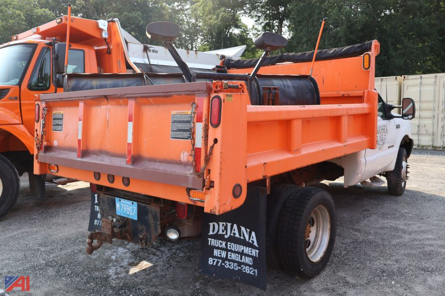 Dump truck bed and plow-equipped chassis showing orange dump bed and white cab with Dejana Truck Equipment branding on mudflaps.