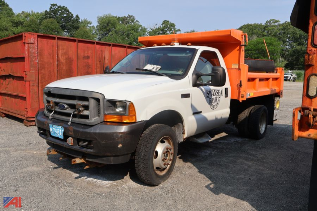Ford F-550 Super Duty dump truck with plow, white cab and orange dump bed, front grille and bumper visible, license plate, and a logo on the door.