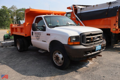Dump truck front-left view showing white cab, orange dump bed, black grille, and front bumper with blue license plate; Ford emblem on grille, company logo on door.