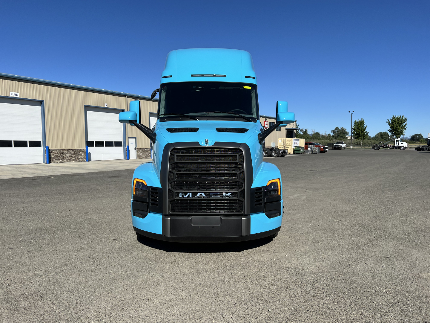 Mack PR64T76H truck front view in blue with large grille and headlights, rating tags visible on windshield area.