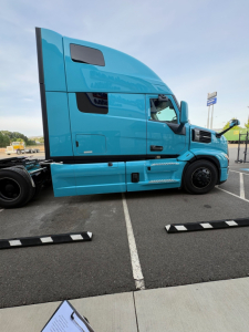 Truck side view of a blue 2027 Mack PR64T76H conventional sleeper tractor with aerodynamic cab and high roof.